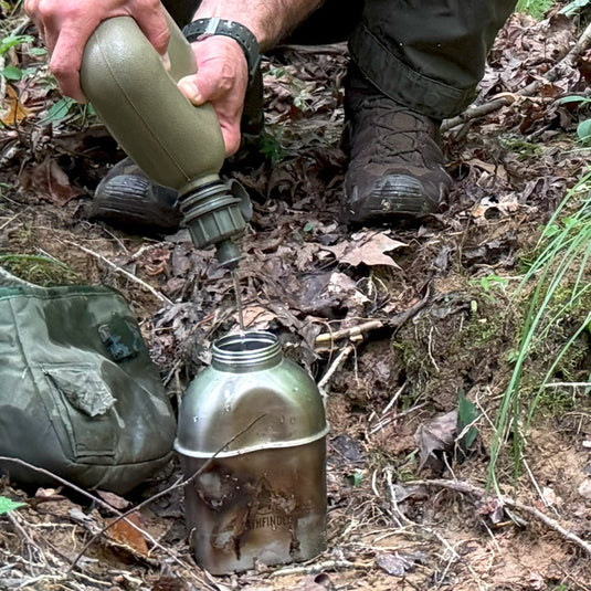A bushcrafter using the 2QT water filter system to squeeze purified water into a canteen