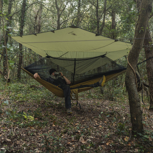 An outdoorsman relaxing in a set up tarp and hammock combo